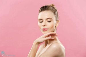 A woman with her hands on her face posing on a pink background.