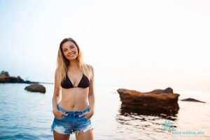 A young woman in a black bikini and denim shorts standing in the water.