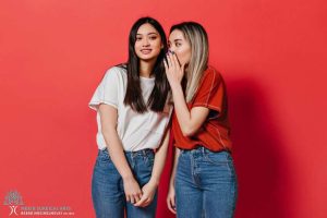 Two young women posing in front of a red background.